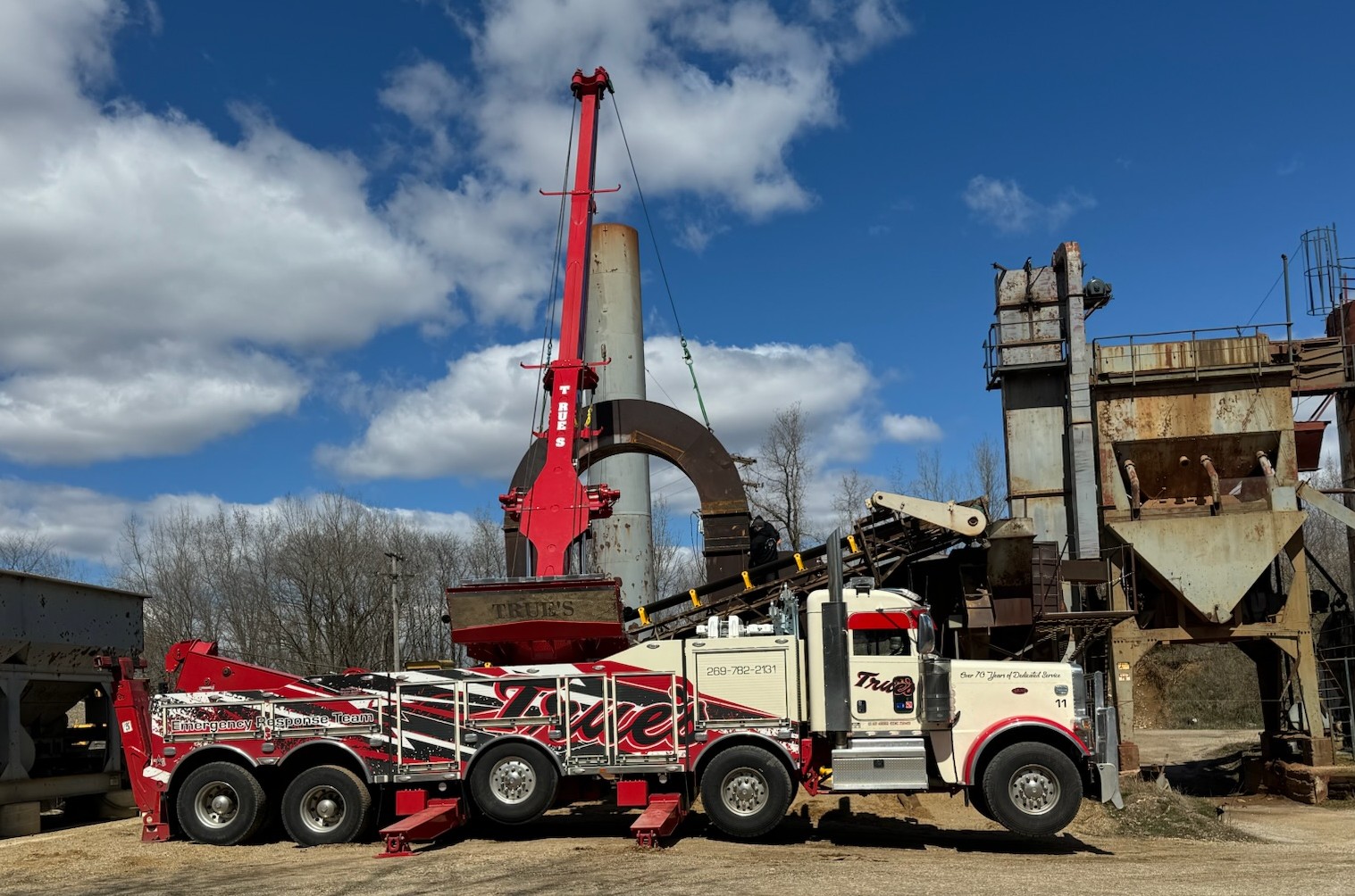 A heavy-duty tow truck using its rotating boom to move a large oil tank.